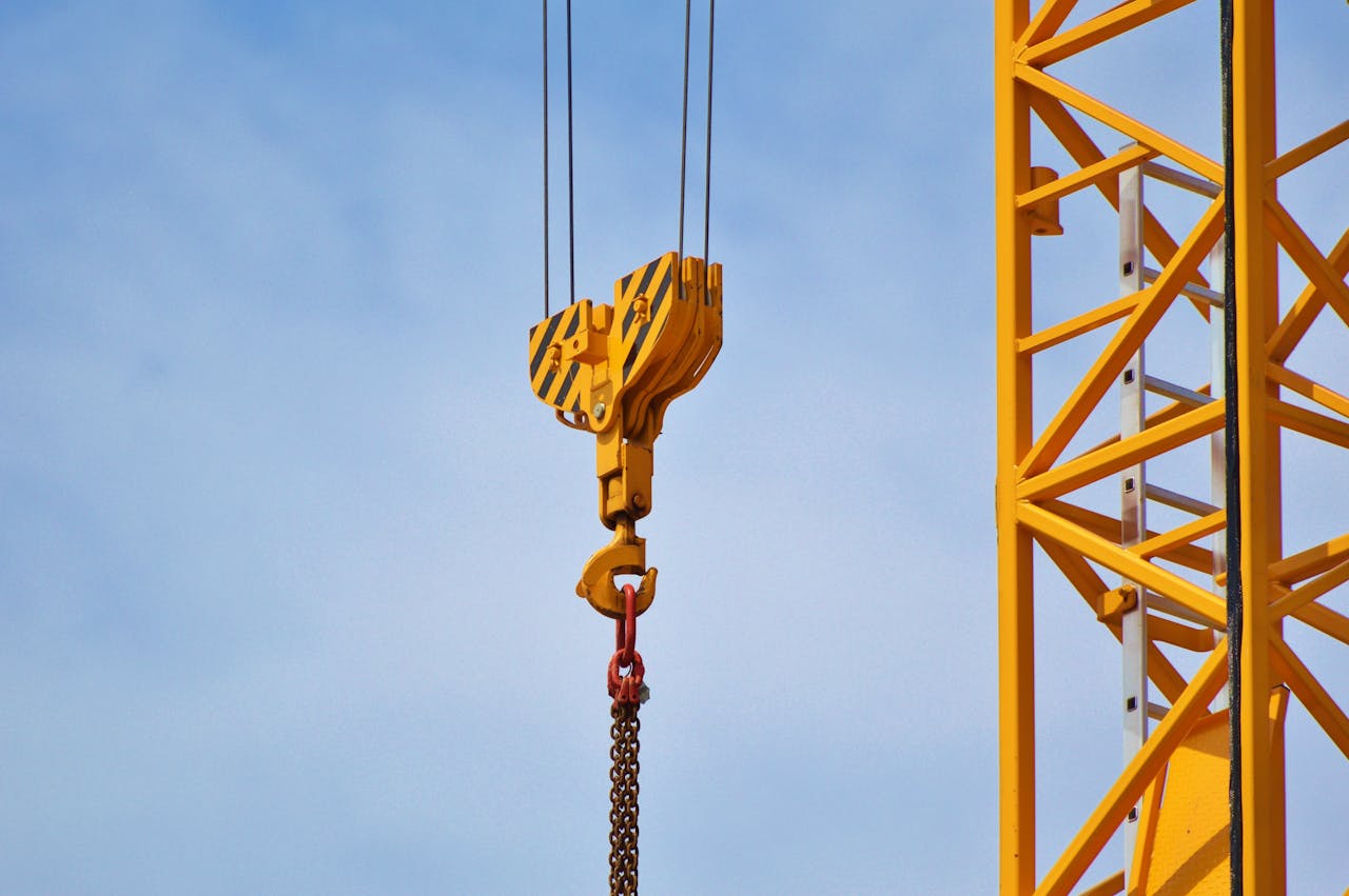 heros-img Close-up of a yellow crane arm against a clear blue sky, showcasing industrial equipment.